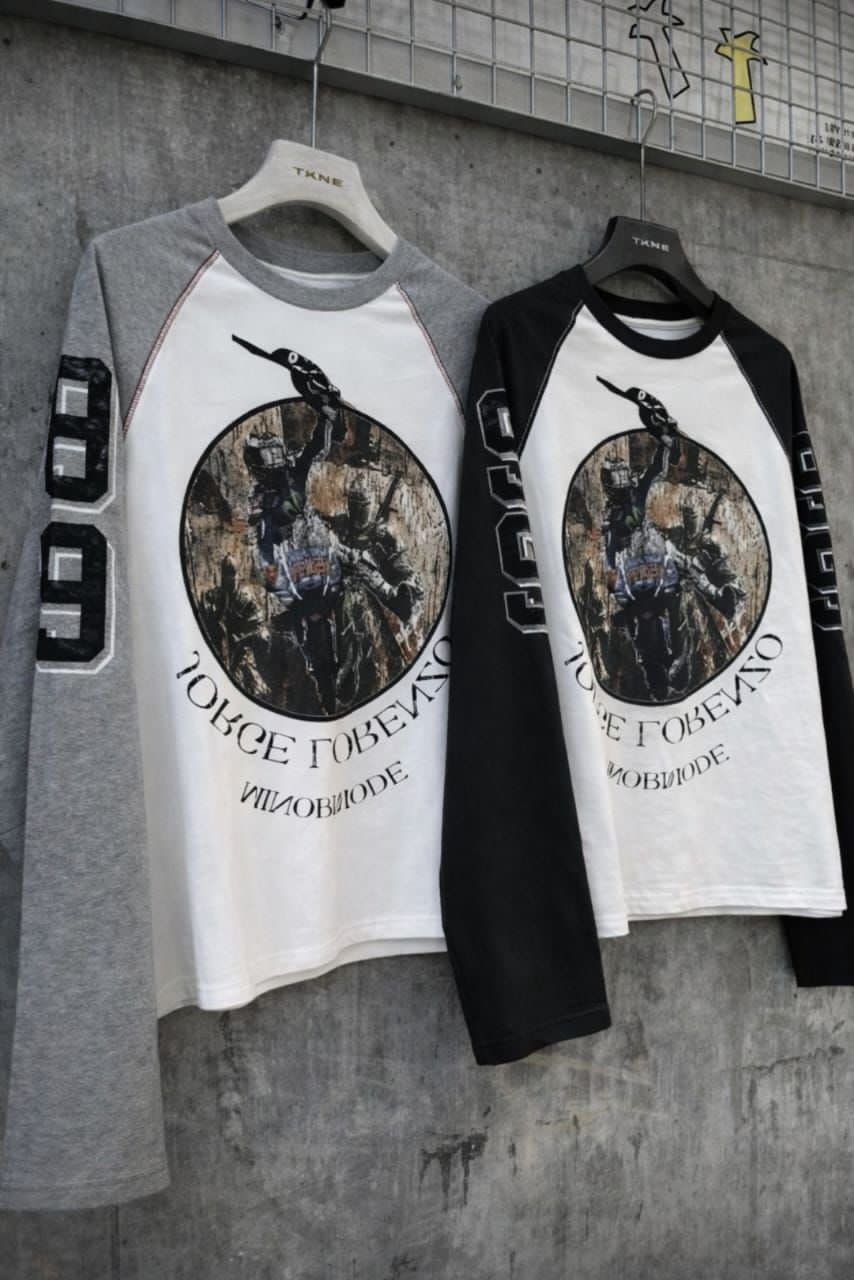 Gray sleeve and black sleeve graphic raglan long sleeve tees hanging against graffiti wall.