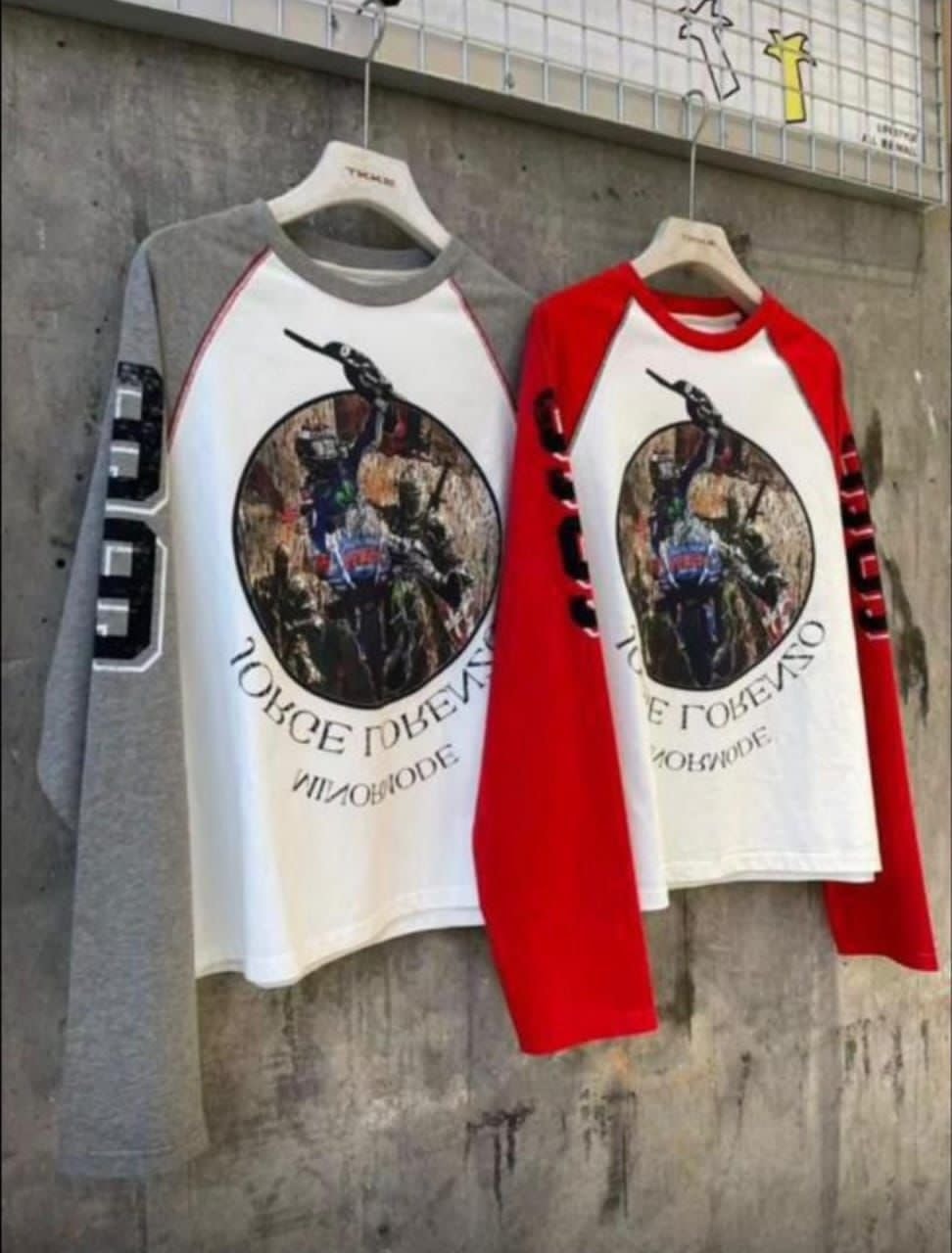 Gray sleeve and red sleeve graphic raglan long sleeve tees hanging against graffiti wall.